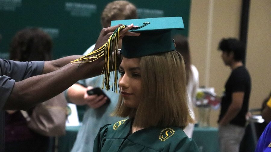 A representative from Candid Campus Pics prepares a student for her cap and gown pictures during Grad Fair. Students could also pick the yearbook and rings during the event.