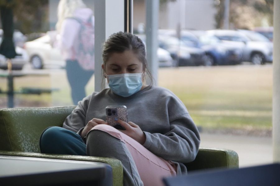 A masked student uses her phone while sitting in the Student Union. Southeasterns mask mandate remains in place for the Spring 2022 semester. Students can self-report COVID-19 symptoms, exposure or infections through the Lion Intervention Network COVID Disclosure Form.