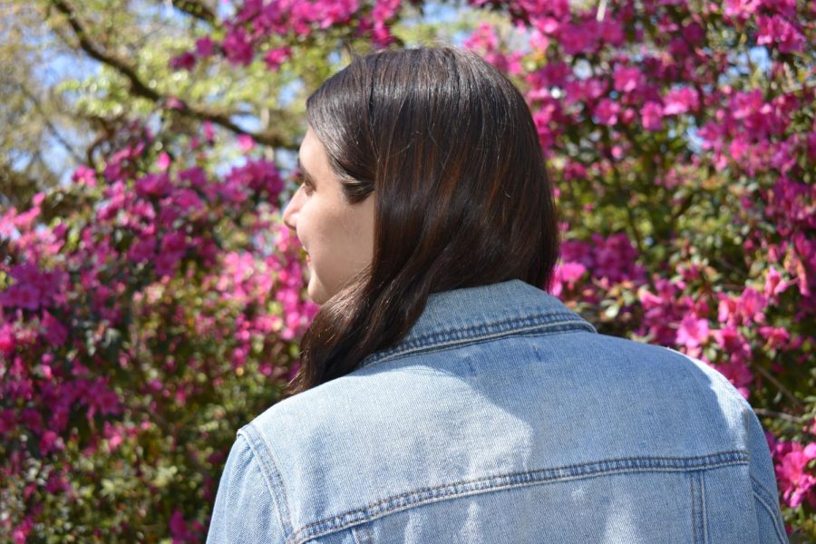Senior communication major Jenna Duvic looks to the side in front of an azalea bush wearing a denim jacket in solidarity with Denim Day. Denim Day originated in 1999 and is a day to bring about the awareness of sexual assault prevention.