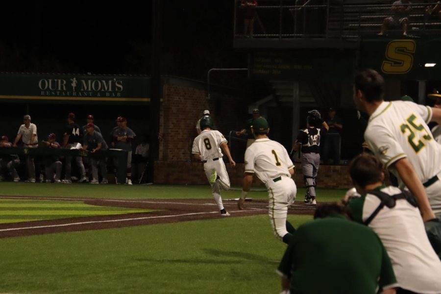Pinch runner Joe Delaney crosses home plate on Tyler Finke's walk-off single as the dugout nears eruption after the Lions 5-4 come from behind win vs Troy on Wednesday night (April 6).