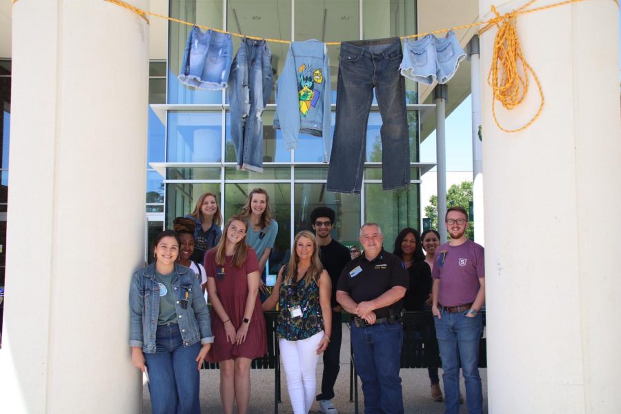 The CARE team stands and poses near their tabling event on campus on April 25. The denim clothing hanging above them is a symbol of breaking the silence for sexual assault survivors. 