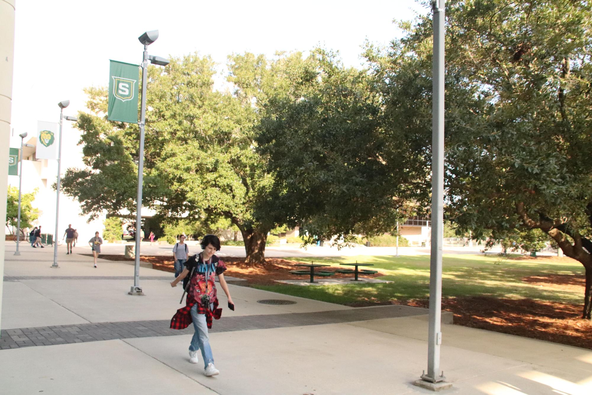 A student walking in front of the union wearing a graphic T-shirt with the addition of red flannel as a belt. 