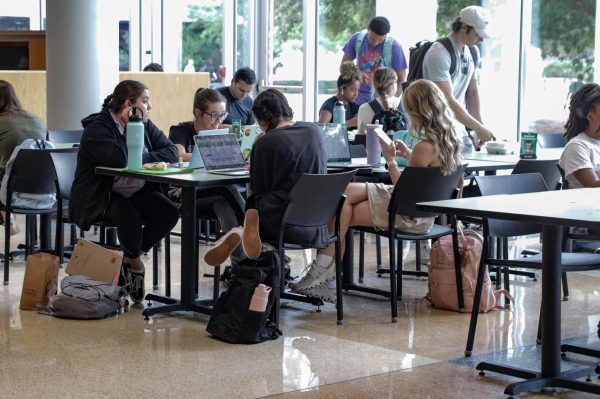 A group of students multi-tasking in the union as they chat and work on their laptops.