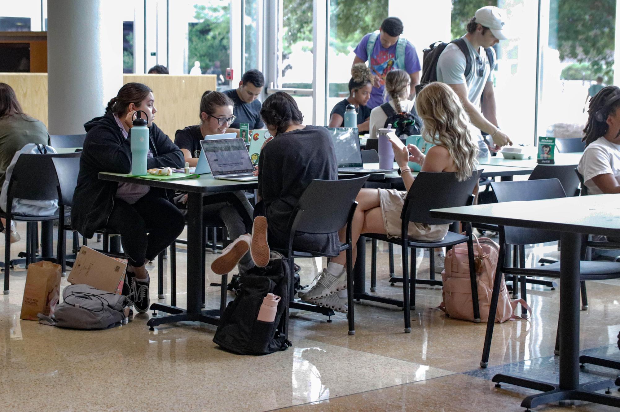 A group of students multi-tasking in the union as they chat and work on their laptops.