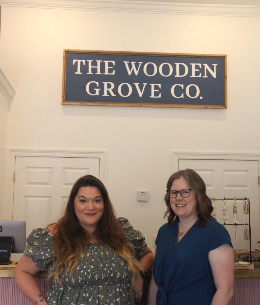 Melissa May, owner of Mel’s Cheesecake, and LeAnne Miller, owner of The Wooden Grove, pose for a photo under The Wooden Grove sign. 