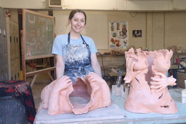 Ava Holloway, a senior ceramics major, posing with pieces of her senior project. Each body of red clay will contain a thematic significance. 