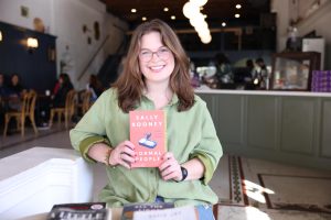 Rebecca Mercante holds up "Normal People" by Sally Rooney while displaying her book at Luma Coffee Roasters in downtown Hammond.