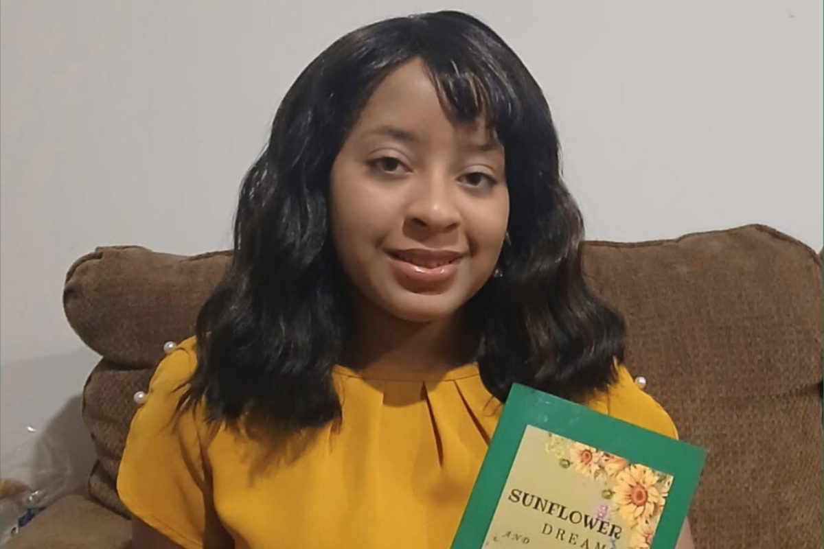 A young woman in a yellow shirt holds up a book with a green border.