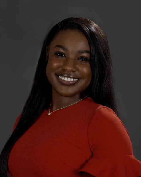 A woman in a red dress poses in front of a dark gray background.