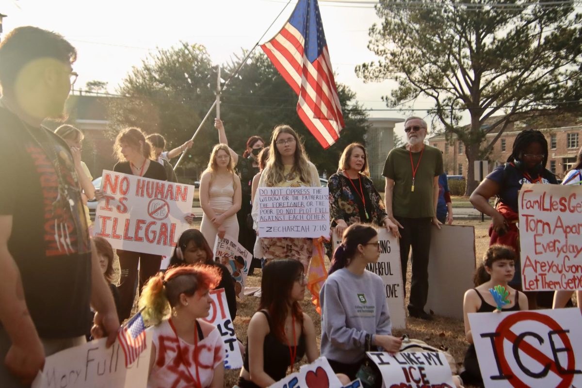 A group of people stand during an organized presentation featuring signs and the American flag.