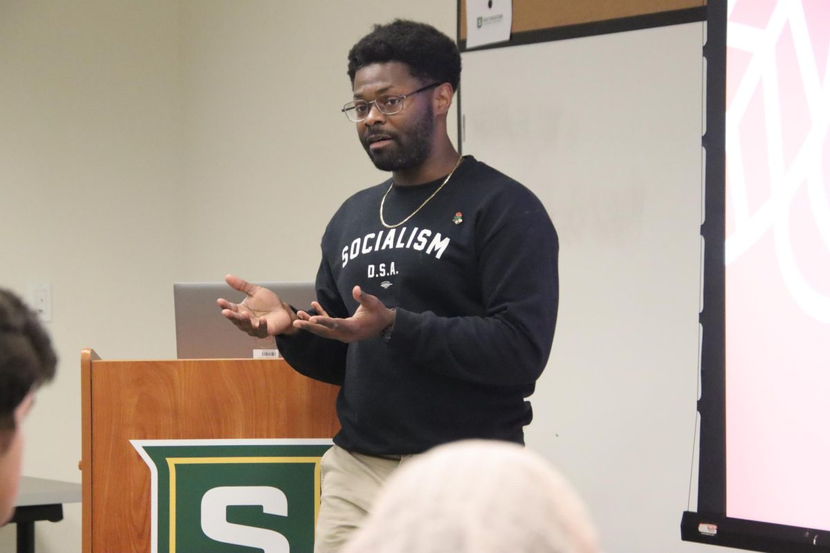 Man speaking in front of attendees at meeting.