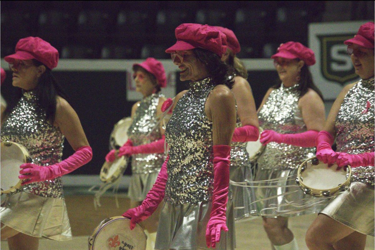 Performers in shiny outfits dance with tambourines.