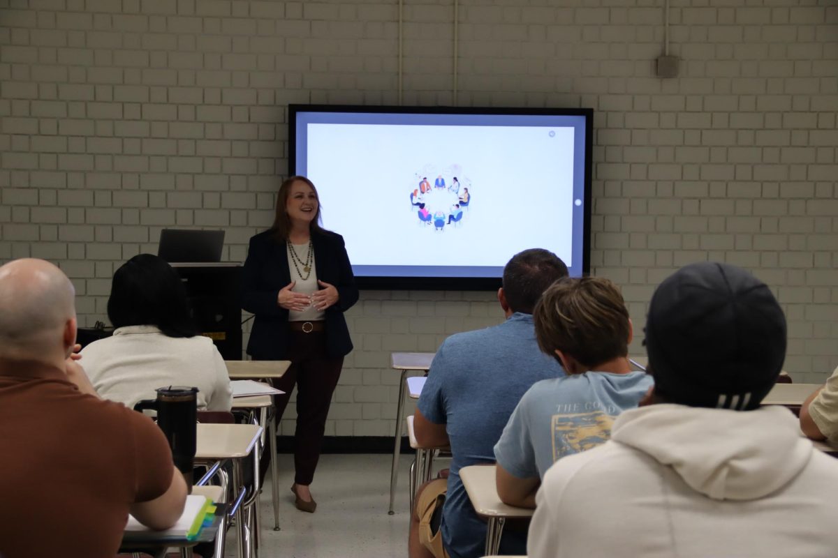 A person stands in front of a screen and talks to a class.