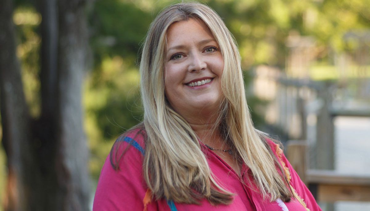A woman in pink stands in front of trees.
