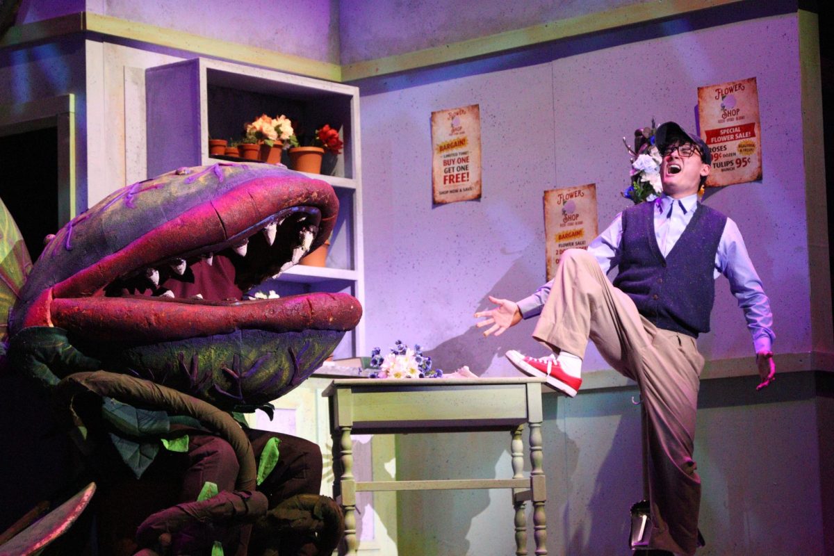 A scared man is spooked by a giant green Piranha plant on a stage.