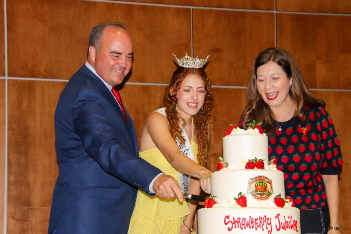 Three people gather around to cut a white cake.